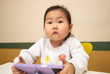 A young girl is sitting at a table with a purple tablet in her hands
