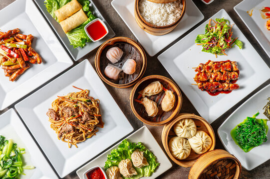Top-down composition of Chinese, Japanese and Asian food with a table full of dishes, spring rolls, beef, noodle dumplings and bao