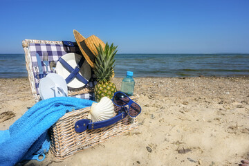 Picnic basket on the beach by the sea with dishes, pineapple, water bottle, towel, straw hat and utensils for swimming vacation in summer, copy space