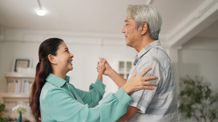 Happy grandfather and grandmother with casual cloth holding hand and dancing together at home. Lovely senior couple moving to music and spending time together while supporting at kitchen. Myrmidon.
