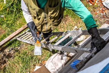 Overhead view of senior Colombian man with gray beard on ladder painting the facade of his farm...