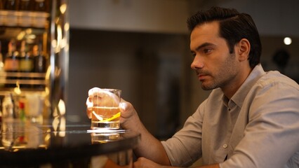 Sitting smart man drinking alone of cocktail Old fashioned waiting friends or couple at bokeh lighting at luxurious beverage counter nightclub at pub and restaurant on Friday meeting night. Vinosity.