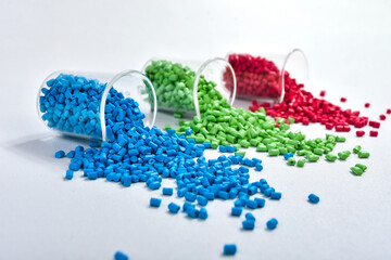 Blue, green and red masterbatch granules spilled from measuring cup, isolated on white background....