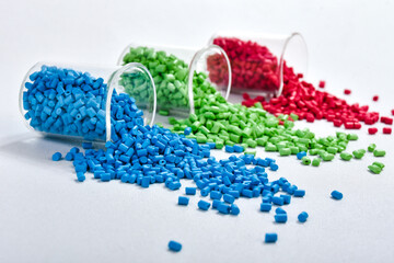 Blue, green and red masterbatch granules spilled from measuring cup, isolated on white background....