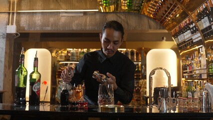 Portrait good looking Asian bartender using jigger measure liquor syrup into mixing glass preparation at luxurious beverage counter bar, neat professional barman costume at nightclub luxury. Vinosity.