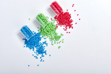 Blue, green and red masterbatch granules spilled from measuring cup, isolated on white background....