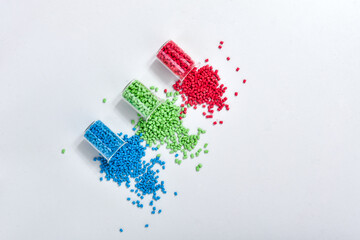 Blue, green and red masterbatch granules spilled from measuring cup, isolated on white background....
