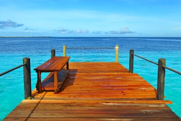 Fototapeta premium Wooden pier and bench with blue ocean in the background. Paradise pier under the tropical sky with azure sea.
