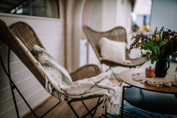  Cozy outdoor seating area with wicker chairs, soft pillows, a throw blanket, and a wooden table with flowers, creating a relaxing atmosphere.
