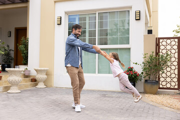 Happy overjoyed Latin dad holding kids hands, lifting flying girl and spinning around, smiling,...