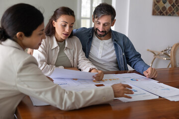 Financial advisor giving consultation to customers, showing analytics on paper diagrams, discussing...