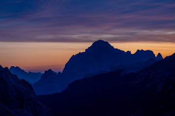 Sunset silhouette of the mountains in the Alps. Dolomites alpine beautiful landscape in red, orange and yellow light of sunset and sunrise, dawn soft light through darkness of the sky in the Dolomiti