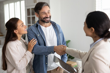 Couple of positive satisfied property buyers giving handshake to female Indian realtor, thanking mortgage broker for help, closing apartment buying deal, smiling, laughing