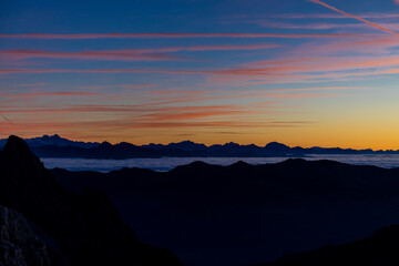 Fototapeta premium Sunset silhouette of the mountains in the Alps. Dolomites alpine beautiful landscape in red, orange and yellow light of sunset and sunrise, dawn soft light through darkness of the sky in the Dolomiti