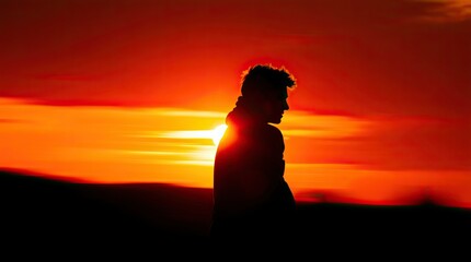 A person walks slowly silhouetted against a stunning sunset filled with vibrant orange and red hues creating a calm and reflective atmosphere during twilight