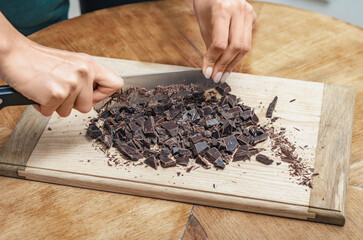 Hands chopping dark chocolate on wooden board background