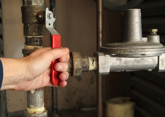 Technician using gas shut-off valve in front of gas pressure regulator. Natural gas boiler supply line for hot water heating. Gas safe, technician or plumbing hot water background. Selective focus.