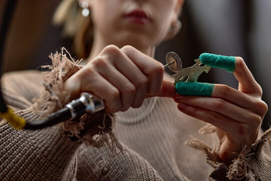 Person carefully preparing tattoo machine, their hands holding green-wrapped tool with focus on detailed adjustment of device in a studio setting