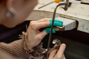 Close-up shot showing precise work while cutting piece of material with jeweler's saw in workshop setting, highlighting craftsmanship and attention to detail