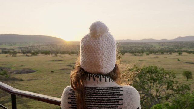 Young woman standing in observation point over rising sun in Serengeti Park. Amazing vast open terrain in African morning. Female tourist enjoys stunning landscape during sunrise. Safari vacation trip