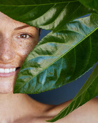 Detox skincare treatments. Organic skin care concept. Close up beauty portrait of young beautiful woman with freckles and red hair is posing with a big fresh green tropical leaf.