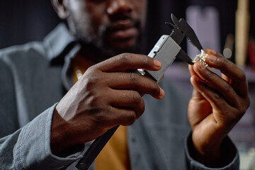 Person meticulously inspecting piece of jewelry using precise measuring tool. Focus is on hands and...