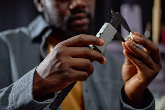 Person meticulously inspecting piece of jewelry using precise measuring tool. Focus is on hands and tool, reflecting fine craftsmanship