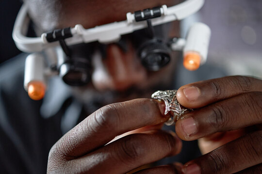Close-up of African American jeweler carefully examining ring using magnifying headset in workshop setting, highlighting precision and attention without distractions - Powered by Adobe