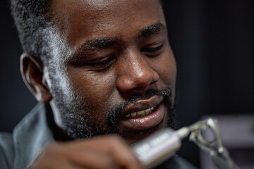 Smiling Black man holding dental care instrument, displaying focused attention on task, with neutral background creating clear focal point on individual