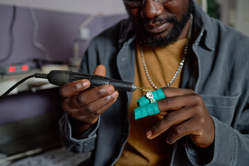 Focused artisan working on creating intricate jewelry piece using precision tools and expertise. Attention given to small details in skilled jewelry-making process