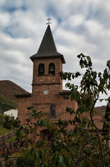 Fototapeta premium Vertical photograph of the parish church of San Gil on a cloudy day, with its facade with pinkish rock, in the village Eugui, Navarra Spain. 