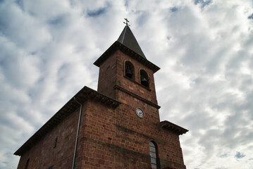 Obraz premium Photograph of the parish church of San Gil on a cloudy day, with its facade with pinkish rock, in the village Eugui, Navarra Spain.