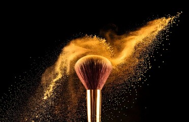 Makeup brush with gold powder explosion against a black background...