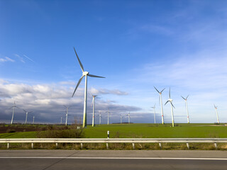 A long row of wind turbines is neatly lined up in a vast field