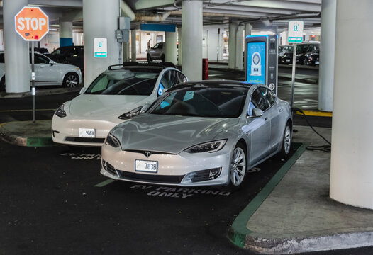 Oahu, Hawaii, USA - February 22, 2024 - Two Tesla vehicles charging at the Ala Moana car parking facility on the ground floor of the largest open-air shopping center in the world.