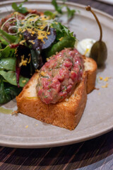 Marinated steak tartar raw beef meat served on bread toasts with green salad in German restaurant