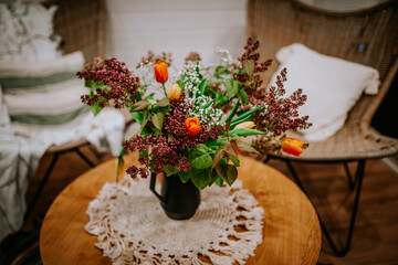 A cozy indoor setting featuring a bouquet of fresh tulips and lilacs in a black vase on a wooden table with a crocheted doily.
