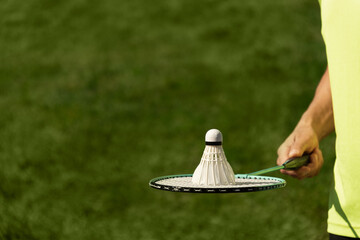 White badminton shuttlecock and badminton racket in man hands. Summer sports game. Outdoor activity. Close up. Copy space.