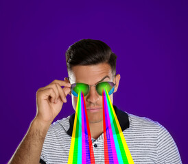 Fashionable man shooting with rainbow lasers out of his eyes through sunglasses on indigo color...
