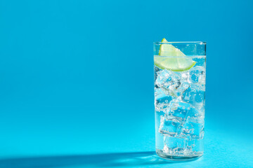Soda water with lime and ice cubes in glass on light blue background, space for text