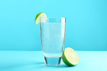 Soda water with lime in glass on light blue background