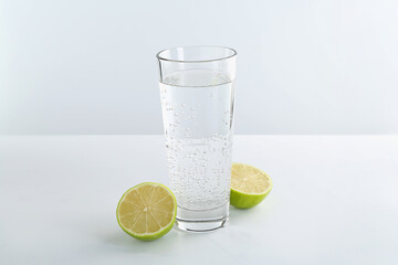 Refreshing soda water in glass and halves of lime on white table against light background