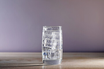 Refreshing soda water with ice cubes in glass on wooden table against grey background