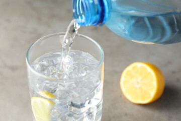 Pouring refreshing soda water from bottle into glass at grey table, closeup