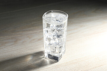 Refreshing soda water with ice cubes in glass on light wooden table, closeup
