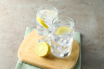 Refreshing soda water with ice cubes and cut lemon in glasses on grey textured table, closeup