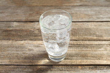 Soda water with ice cubes in glass on wooden table, closeup