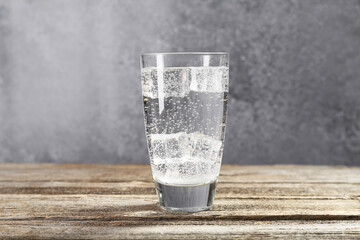 Soda water with ice cubes in glass on wooden table