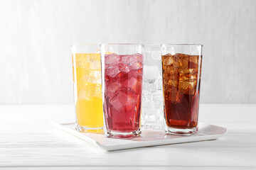 Soda water of different flavors with ice cubes in glasses on white wooden table