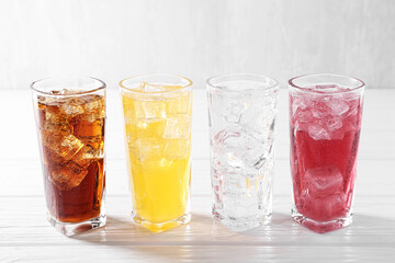 Soda water of different flavors with ice cubes in glasses on white wooden table